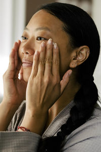 Young woman applying moisturizer on face at home