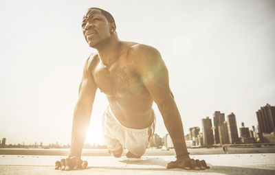 Full length of shirtless man standing against sky in city