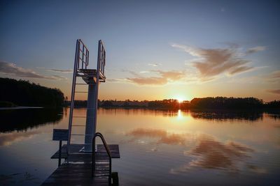 Silhouette of diving platform by lake against sky during sunset