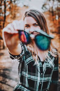 Portrait of beautiful woman holding camera while standing outdoors