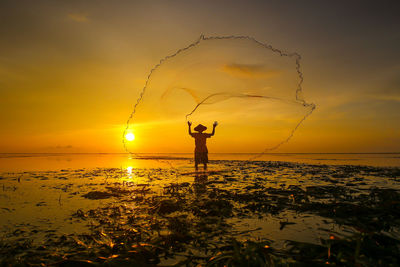 Silhouette man fishing in sea against sky during sunset