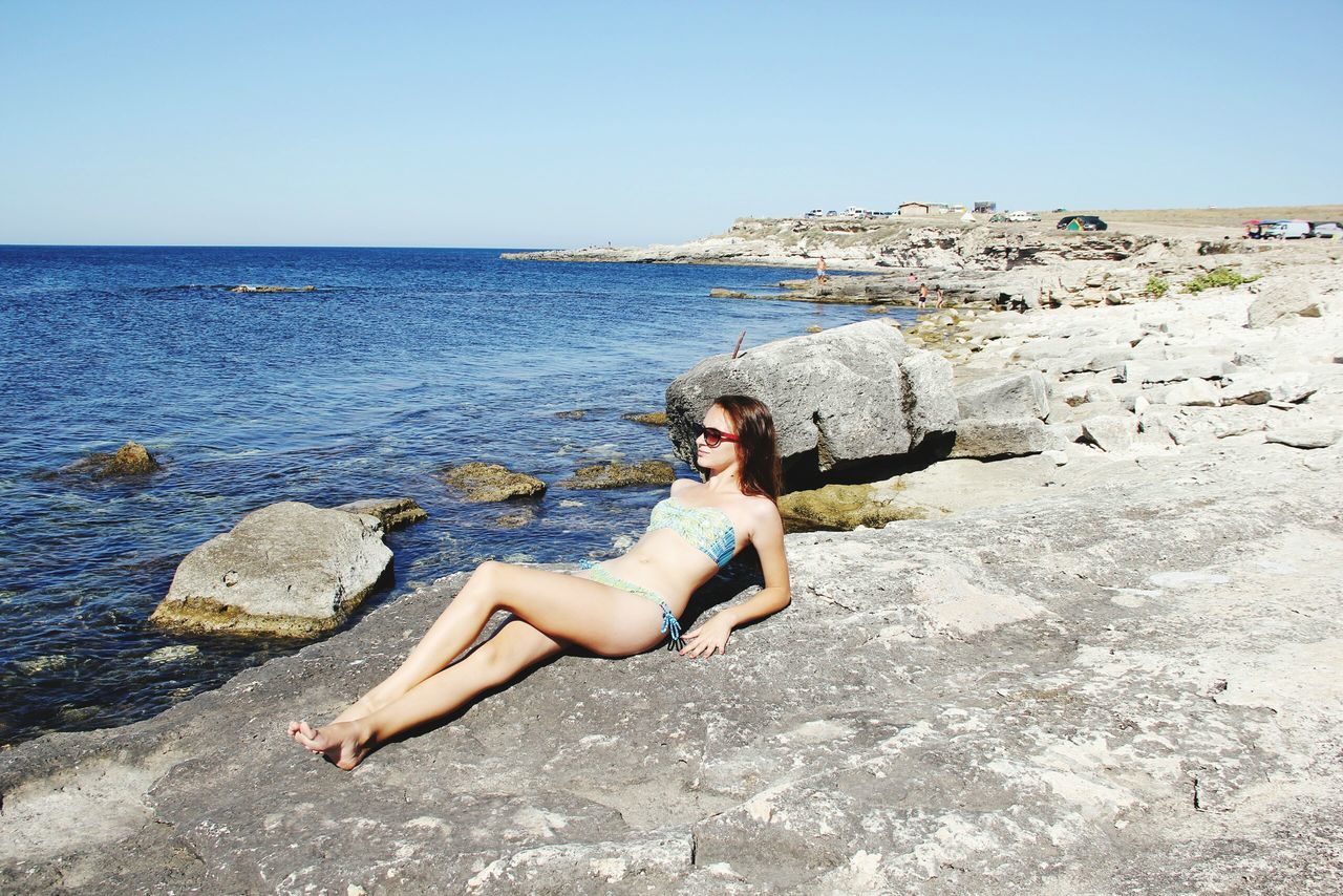 sea, young adult, beach, lifestyles, young women, leisure activity, water, person, shore, horizon over water, full length, sitting, clear sky, sand, vacations, casual clothing, relaxation, sunlight