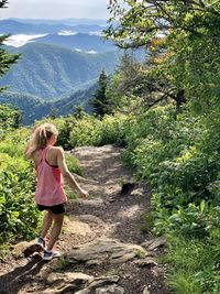 Rear view of woman walking on dirt road against landscape