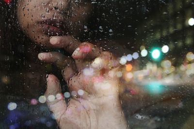 Midsection of woman seen through wet glass window during rainy season at night