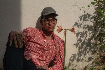 Portrait of young man with grey leather cap sitting against wall