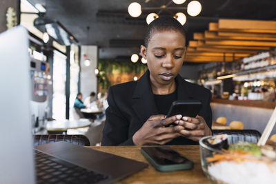 Businesswoman using smart phone at table in cafe