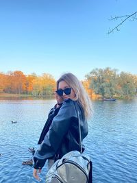 Portrait of young woman standing by lake against clear sky