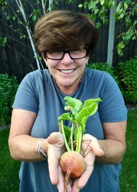 Portrait of smiling woman holding root vegetable at yard