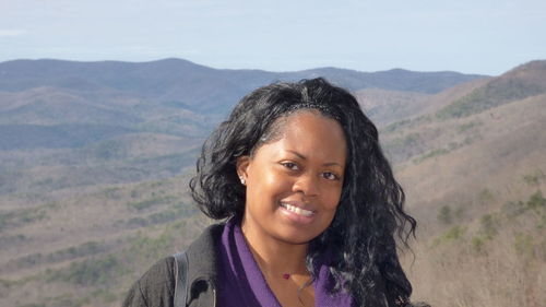 Portrait of smiling woman standing on mountain against sky