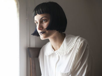 Young woman looking away while sitting by window