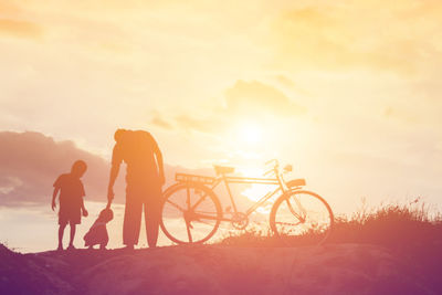 Silhouette men standing by bicycle against sky during sunset