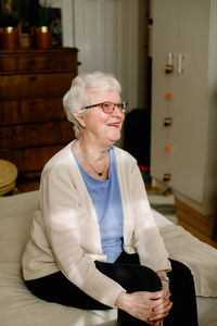 Smiling retired senior woman sitting on bed looking away in nursing home