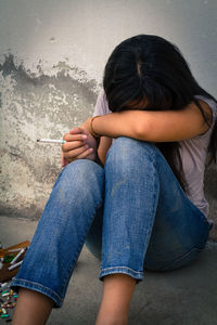 Depressed woman with cigarette sitting by wall
