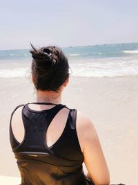 Rear view of woman standing at beach against sky