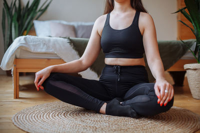 A young woman  sits at home on a jute rug near the bed in the lotus position. does yoga at home.