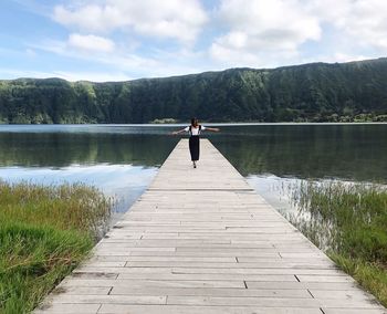 Rear view of man walking on pier over lake against sky