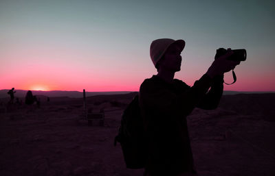 Silhouette man photographing with camera at sunset