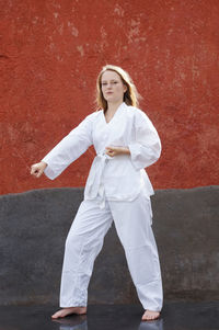 Full length portrait of woman practicing karate against red wall