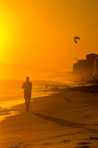 Silhouette man standing on beach against clear sky during sunset