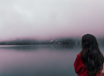 Rear view of woman looking at lake against sky