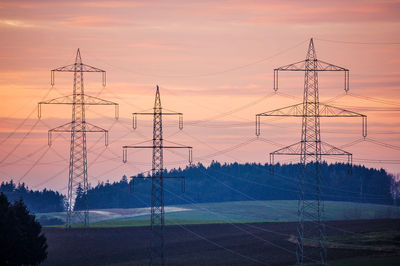 Electricity pylon on landscape against sky at sunset