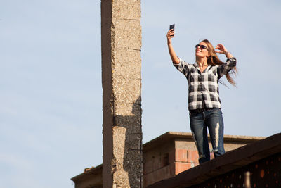 Low angle view of smiling woman talking selfie on terrace