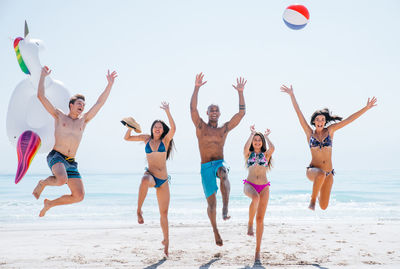 Happy friends jumping on shore of beach against sky