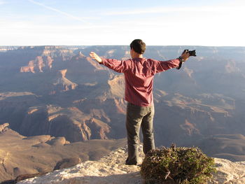 Rear view of man with arms outstretched standing on landscape