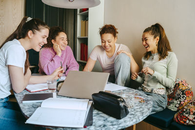 Cheerful female friends studying together while doing homework