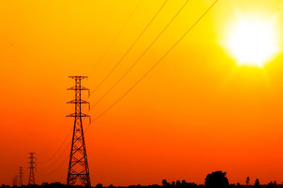 Low angle view of silhouette electricity pylon against orange sky