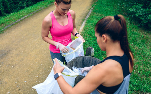 Female friends putting garbage in trash can at park