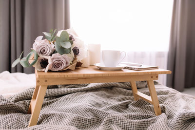 Romantic morning. wooden coffee table with flowers on bed with plaid, coffee cup, candles