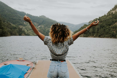 Rear view of woman with arms raised standing on pier over lake