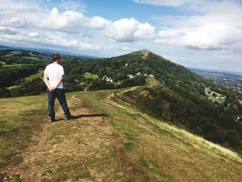 Rear view of man walking on mountain against cloudy sky