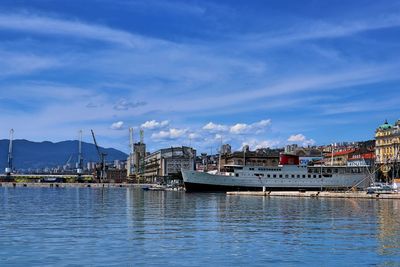 Boats moored on river by buildings against blue sky