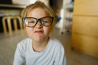 Funny girl with glasses, grimacing at home, looking into camera