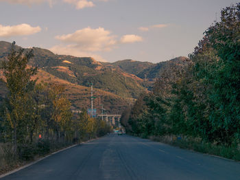 Road amidst trees and mountains against sky