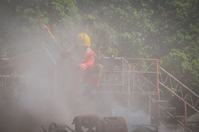 Firefighter with work tool looking at smoke while crouching at footbridge