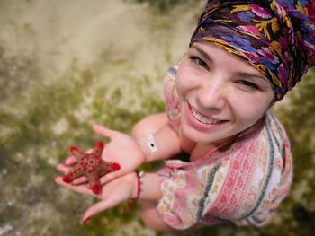 High angle portrait of smiling young woman holding starfish