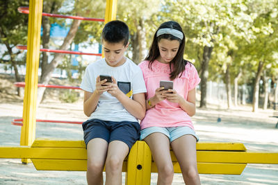 Siblings using phones while sitting outdoors