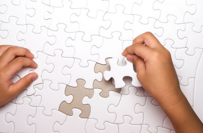 Cropped image of hand holding paper against white wall