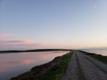 Road by sea against sky during sunset