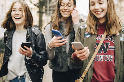 Midsection of female friends using mobile phone while walking in city