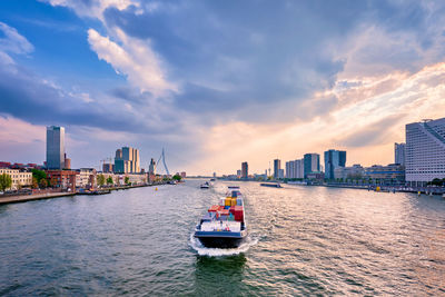 Boats in river by buildings in city against sky