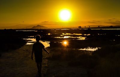 Rear view of silhouette man walking on shore against sunset