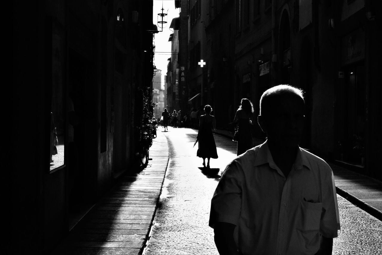 REAR VIEW OF MEN WALKING ON STREET AMIDST BUILDINGS