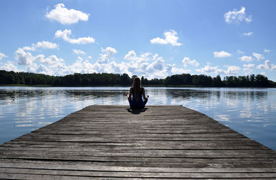 Woman on pier over lake against sky