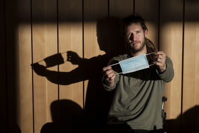 Portrait of man holding mask standing against wall