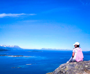 Woman sitting on rock by sea against blue sky