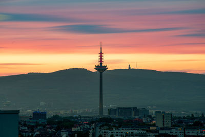 Communications tower in city against romantic sky at sunset